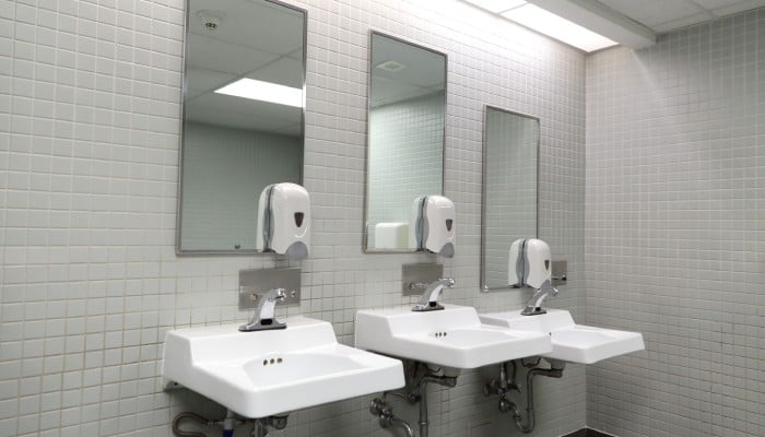 An empty commercial restroom. Three sinks—complete with mirrors and automatic soap dispensers—line the walls.